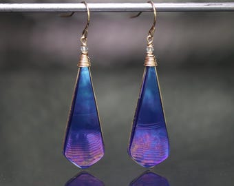 May include: A pair of dangle earrings with iridescent purple teardrop-shaped glass beads and gold wire accents.