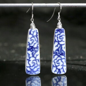 May include: A pair of dangle earrings with a white and blue floral pattern. The earrings have a rectangular shape with a silver wire hook. The blue floral design is a repeating pattern on the white background.