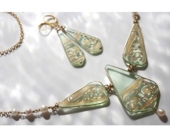 May include: A green glass necklace and earrings set with gold accents. The necklace features a geometric design with a pearlescent chain. The earrings are teardrop shaped with a gold hook.