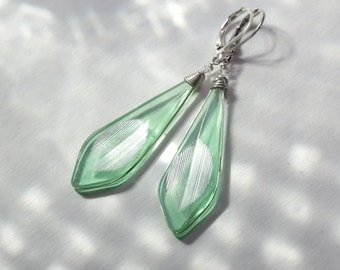 May include: A pair of silver dangle earrings with light green faceted glass drops. The glass has a subtle white pattern.