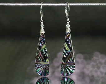 May include: A pair of long, teardrop-shaped earrings featuring a dark, iridescent finish with geometric patterns. The earrings are suspended from silver-toned lever-back hooks, with a small clear bead accent above the main teardrop component.