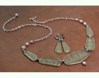 May include: A jewelry set consisting of a necklace and matching earrings. The necklace features a silver chain with small white pearls and five pale green, trapezoidal glass pendants with embossed swirl patterns. Two matching earrings are included.