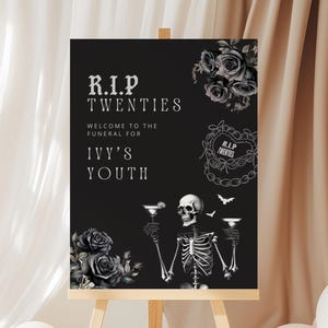 Pode incluir: Uma placa preta em um cavalete de madeira com o texto "R.I.P. TWENTIES" e "WELCOME TO THE FUNERAL FOR IVY'S YOUTH". A placa apresenta um esqueleto segurando coquetéis, rosas e morcegos. Balões brancos e bege em primeiro plano.