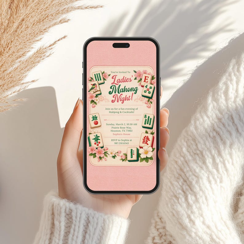 K&ouml;nnte beinhalten: Ein Smartphone zeigt eine rosa Einladung f&uuml;r eine "Ladies Mahjong Night!". Die Einladung enth&auml;lt florale Akzente und Mahjong-Steine. Der Text enth&auml;lt Eventdetails wie Datum, Uhrzeit, Ort und RSVP-Informationen. Das Telefon wird von einer Person gehalten.