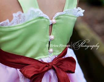 May include: A green and white dress with a red bow and pearl buttons. The dress has a lace trim and a pink skirt.