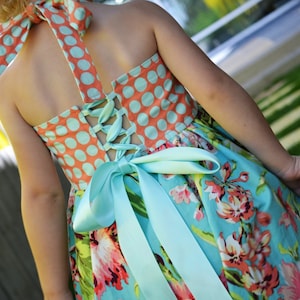 Peut inclure: Une robe à pois bleus et oranges avec un dos en dentelle blanche et un ruban bleu assorti noué en un nœud à la taille.