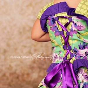 Peut inclure: Une robe florale verte et violette avec un ruban violet lacé dans le dos. La robe a un ourlet à volants et un corsage ajusté.