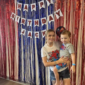 Puede incluir: Una mujer y un ni&ntilde;o frente a una cortina de l&aacute;minas rojas, blancas y azules. Una pancarta dice "HAPPY BIRTHDAY JACK". La mujer y el ni&ntilde;o llevan camisetas. El ni&ntilde;o lleva una camiseta de Spider-Man.