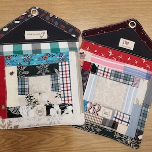 Könnte beinhalten: Zwei handgefertigte, gesteppte Topflappen in Hausform. Sie bestehen aus einem Patchwork aus Stoffresten in verschiedenen Mustern, darunter Blumen- und Karomuster. Einer hat ein Etikett mit der Aufschrift "made by hand", der andere mit "I love handmade".