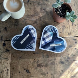 Könnte beinhalten: Zwei herzförmige Stoffuntersetzer mit einem Patchwork-Design in Blau- und Weißtönen. Jeder Untersetzer hat einen weißen Rand und den Text "Happy everyday". Eine Tasse Kaffee und eine kleine Topf-Sukkulente sind ebenfalls zu sehen.