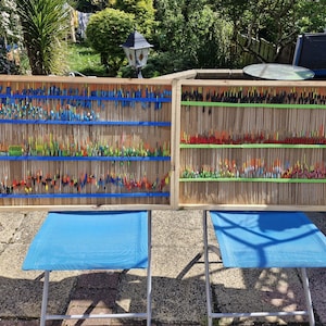 Può includere: Due cornici in legno piene di file di galleggianti da pesca in vetro colorati. Le cornici sono appoggiate su sedie pieghevoli blu davanti a un prato verde.