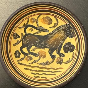 May include: A decorative ceramic plate featuring a black lion design on a yellow background. The lion is surrounded by floral and water motifs. The plate has a dark brown rim with concentric brown and black bands. A unique piece for home decor.