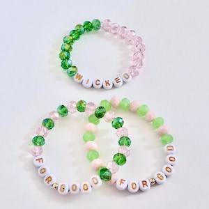 May include: Three beaded bracelets with the words "WICKED" and "FOR GOOD" spelled out in white letter beads. The bracelets feature green and pink crystal beads. One bracelet is green and pink, and the others are green and pink.