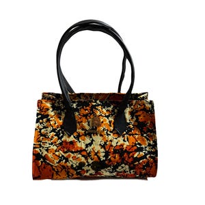 May include: A small handbag with a colorful pattern in shades of orange, black, and cream. The bag has black leather handles and trim. The bag is rectangular with a button closure.