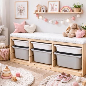 May include: A light wood storage bench with three compartments, each holding a white and gray bin. The bench is in a child's room with pink and white decor, including a rug, pillows, and a stuffed bunny.