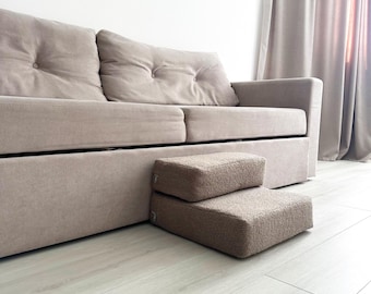 May include: A two-step pet stair in a neutral beige color, positioned in front of a beige sofa. The stairs are made of a soft, textured material, providing a comfortable and accessible way for pets to reach the sofa.