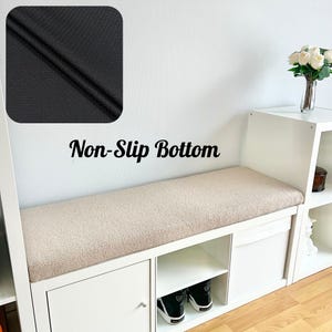Puede incluir: Banco de almacenamiento blanco con cojín beige y base antideslizante negra. El banco tiene múltiples compartimentos de almacenamiento y se ve un par de zapatillas deportivas blancas y negras. El texto "Non-Slip Bottom" está en la pared.