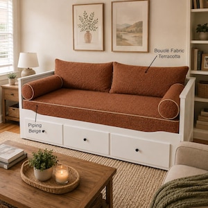 Peut inclure: Un lit de repos blanc avec trois tiroirs de rangement et un coussin en tissu bouclé terracotta. Le lit de repos comprend deux coussins traversins cylindriques avec un passepoil beige. Des étiquettes indiquent Bouclé Fabric Terracotta et Piping Beige.