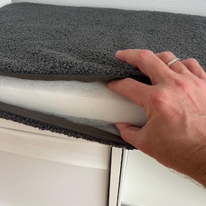 May include: A gray, textured cushion cover with a zipper, revealing a white foam interior. The cover has a plush, shaggy appearance. The cushion is designed for comfort and support.