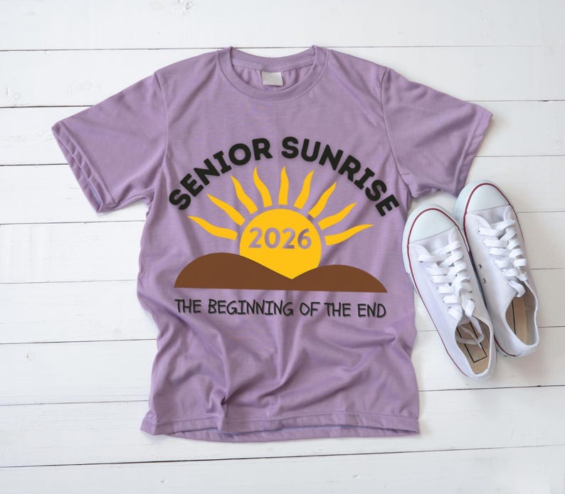 May include: A lilac-colored t-shirt with the words "SENIOR SUNRISE 2026" in black and yellow, featuring a sun graphic. Below the graphic is the phrase "THE BEGINNING OF THE END." White sneakers are placed next to the shirt.