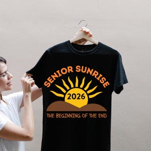 May include: Black t-shirt with the words "SENIOR SUNRISE 2026" in orange and yellow. The design features a sun graphic above a brown line, with the phrase "THE BEGINNING OF THE END" below.