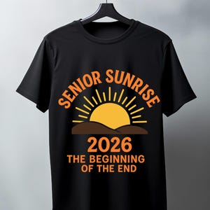 May include: Black t-shirt with the words "SENIOR SUNRISE" in orange arched above a yellow sun graphic. Below the sun is the year "2026" and the phrase "THE BEGINNING OF THE END" in orange. The shirt is hanging on a black hanger.