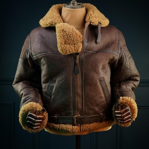 Puede incluir: Chaqueta de cuero marrón con cuello y puños de borrego. La chaqueta tiene cierre de cremallera, cinturón en la cintura y dos bolsillos delanteros. Se exhibe en un maniquí.