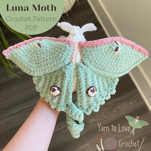 Peut inclure: Un patron de crochet de papillon de lune fait à la main, aux couleurs vert sauge, rose et blanc. Le papillon a des ailes détaillées et un corps texturé. Le texte "Sage the Luna Moth Crochet Pattern PDF" est inclus.