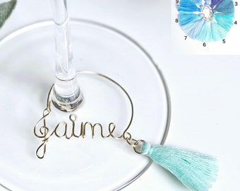 May include: Gold wire wine glass charm with the word "Jaime" and a light blue tassel.