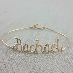 May include: Gold wire bracelet with the name "Rachael" spelled out in cursive.