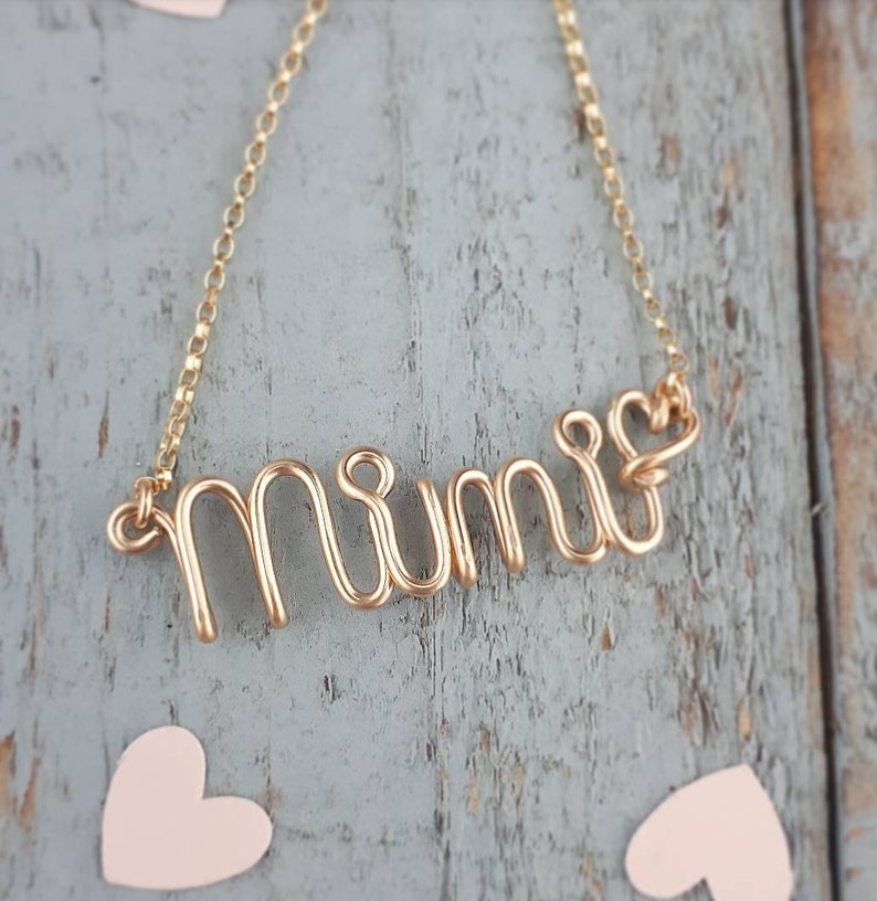 May include: Gold necklace with the word "Mimi" spelled out in wire. The necklace has a heart charm at the end.