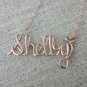 Pode incluir: Um colar de ouro rosa com o nome "Shelly" escrito em arame.