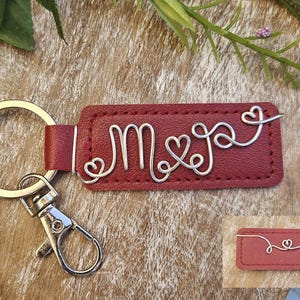 May include: A burgundy leather keychain with silver wire initials "M & J" and heart accents. The keychain has a silver keyring and clasp. A smaller version of the keychain is also visible.
