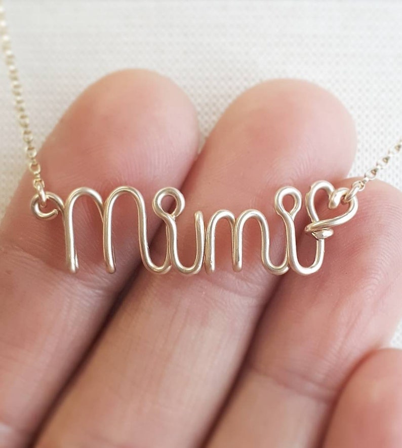 May include: Gold wire necklace with the word "Mimi" spelled out in a delicate, cursive style.