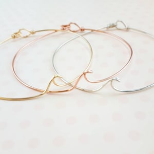 May include: Three delicate wire bracelets with a wave design. The bracelets are gold, rose gold, and silver.