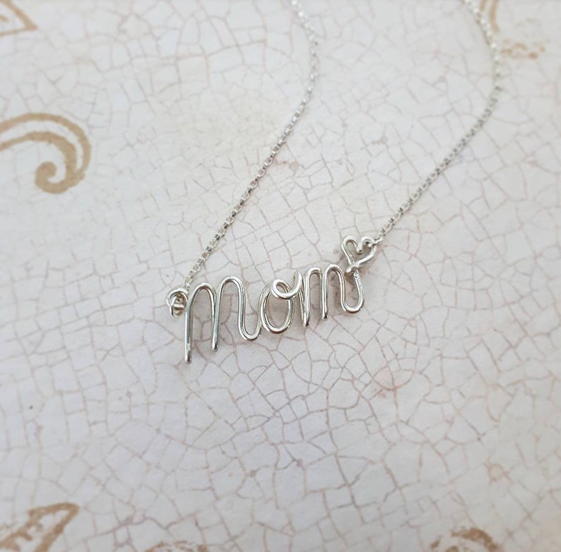 May include: Silver necklace with the word "MOM" spelled out in wire, with a small heart charm at the end.
