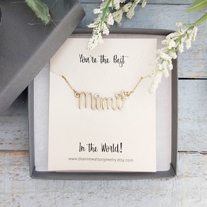 May include: A gold-colored wire necklace spelling "Mimi" in cursive, presented in a gray gift box. The necklace is on a card with the text "You're the Best" and "In the World!". The Etsy shop URL is also visible.