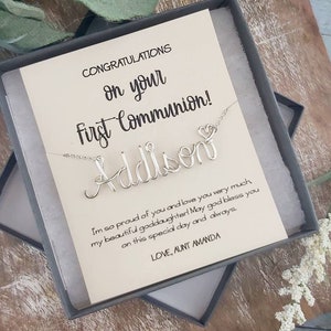 May include: A white card with the text "CONGRATULATIONS on your First Communion!" and the name "Addison" written in cursive with a heart. The card is in a gray box with a silver necklace with the name "Addison" written in cursive with a heart.