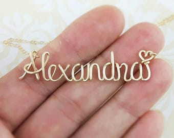 May include: Gold wire necklace with the name "Alexandra" spelled out in cursive with a small heart charm at the end.