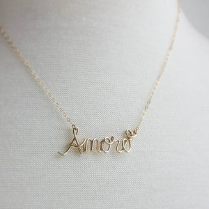 Pode incluir: Um colar de ouro com a palavra "Amore" escrita em cursivo. O "e" de Amore tem a forma de um cora&ccedil;&atilde;o.