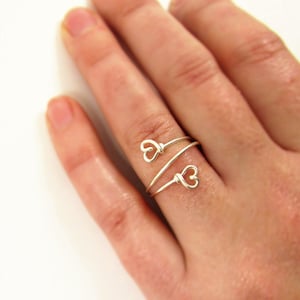 May include: A silver ring with two heart-shaped wire designs. The ring is wrapped around a finger.