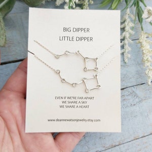 May include: A white card with the text "BIG DIPPER LITTLE DIPPER" and the text "EVEN IF WE'RE FAR APART WE SHARE A SKY WE SHARE A HEART" and the website address "www.deannewatsonjewelry.etsy.com". The card has two silver necklaces with the Big Dipper and Little Dipper constellations.