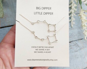 May include: A white card with the text "BIG DIPPER LITTLE DIPPER" and the text "EVEN IF WE'RE FAR APART WE SHARE A SKY WE SHARE A HEART" and the website address "www.deannewatsonjewelry.etsy.com". The card has two silver necklaces with the Big Dipper and Little Dipper constellations.