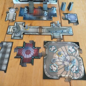 Puede incluir: Un juego de mesa con losetas modulares con patrones de cuadrícula, varias figuras en miniatura de plástico gris y piezas de terreno en 3D. Las losetas representan entornos de ciencia ficción con diseños de suelo metálicos, rojos y beige.