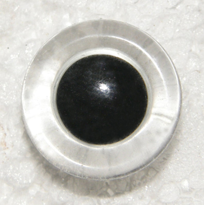 May include: A clear plastic eye with a black pupil, commonly used for craft projects.