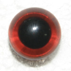 May include: A close-up of a red glass eye with a black pupil. The eye is shiny and reflective.