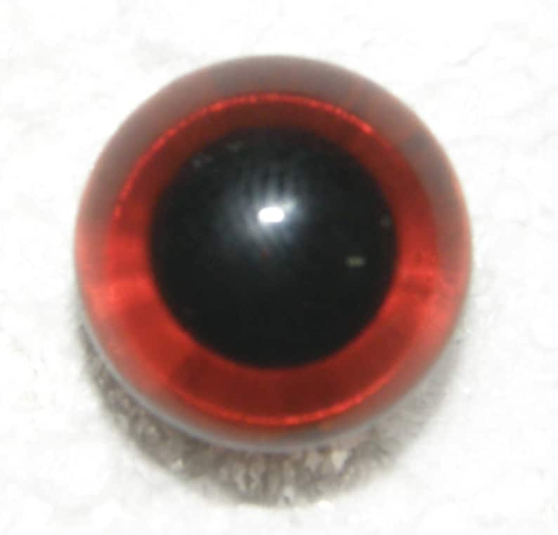 May include: A close-up of a red glass eye with a black pupil. The eye is shiny and reflective.