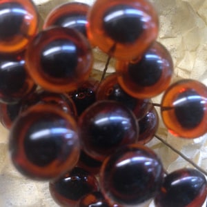 May include: A close-up of a group of brown glass eyes with black pupils. The eyes are arranged in a cluster and appear to be for craft projects.