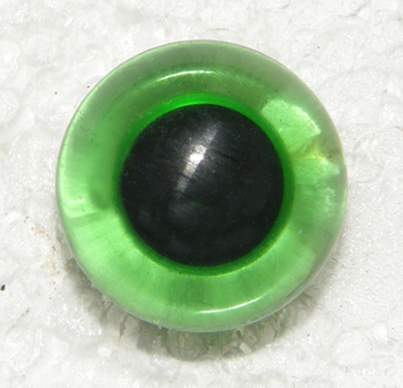 May include: A green plastic eye with a black pupil. The eye is shiny and has a raised rim.