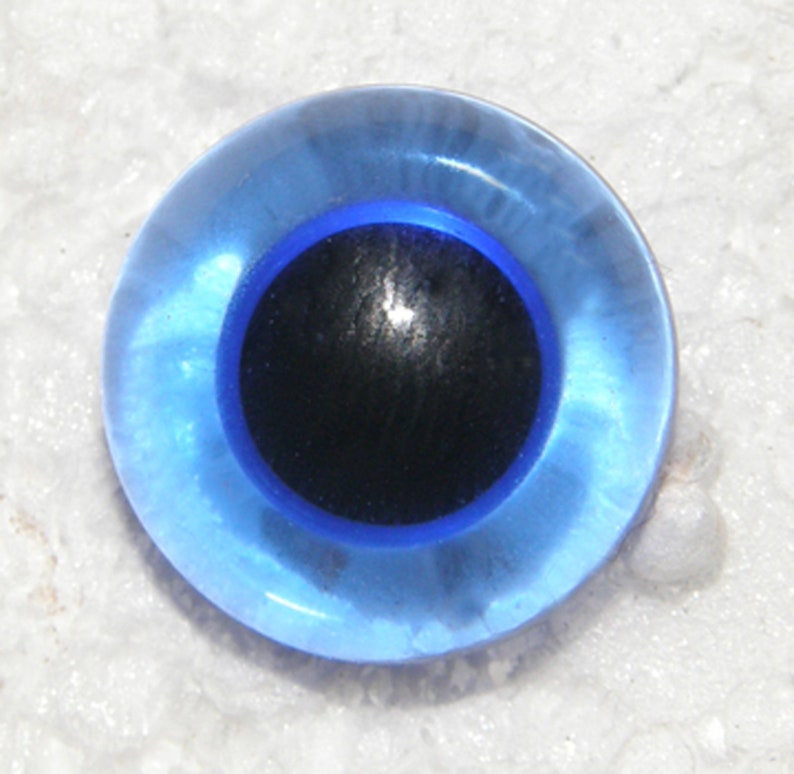 May include: A blue plastic googly eye with a black pupil. The eye is round and has a shiny finish.
